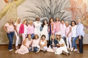 Group of breast cancer survivors posing together in pink, white, and pastel clothing in front of a floral mural.
